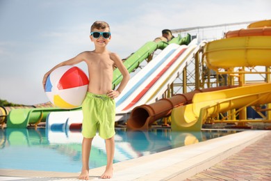 Cute little boy with inflatable ball near pool in water park, space for text