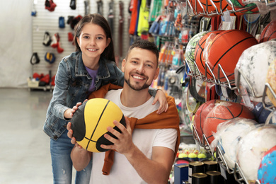 Little school girl with father choosing ball in supermarket