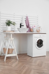 Photo of Laundry room interior with modern washing machine and stylish vessel sink on white wooden countertop