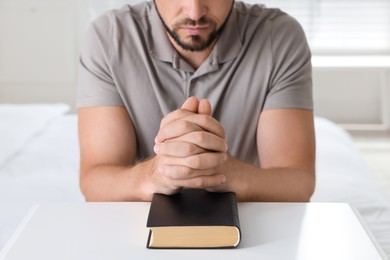 Religious man with Bible praying at home, closeup