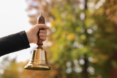 Pupil holding school bell outdoors on sunny day, closeup. Space for text