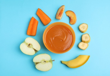 Baby food in bowl and fresh ingredients on light blue background, flat lay