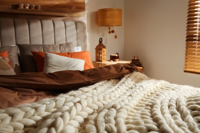 Bed with knitted blanket and cushions in room. Interior design