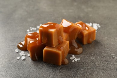 Photo of Yummy caramel candies with sauce and sea salt on grey table, closeup