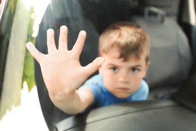 Upset little boy closed inside car, closeup with space for text. Child in danger