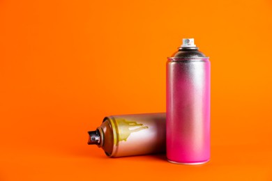 Photo of Used cans of spray paint on orange background. Space for text