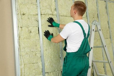 Worker installing thermal insulation material on wall indoors
