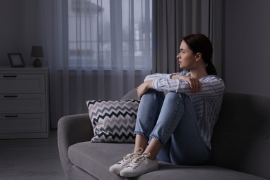 Unhappy young woman on sofa at home, space for text. Loneliness concept