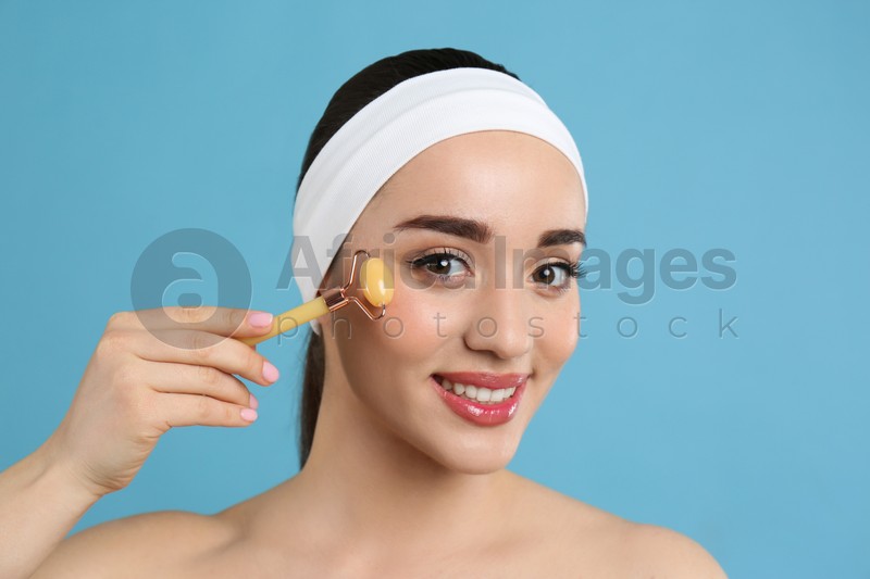 Photo of Woman using natural face roller on light blue background