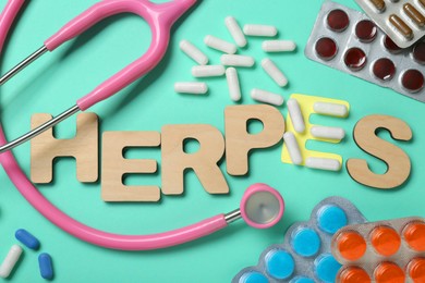Word Herpes made of wooden letters, different pills and stethoscope on turquoise background, flat lay