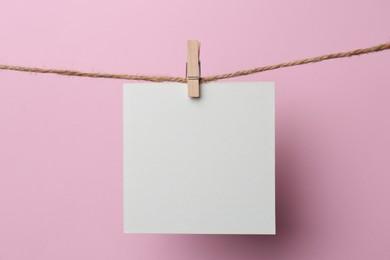 Wooden clothespin with blank notepaper on twine against pink background. Space for text