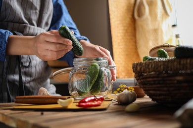 Woman putting cucumbers into jar at wooden table, closeup. Pickling vegetables