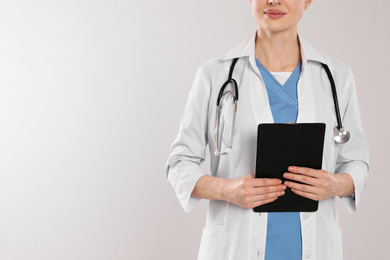 Doctor with stethoscope and clipboard on light grey background, closeup. Space for text
