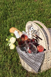 Picnic basket with tasty food, flowers and cider on grass