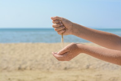 Photo of Child pouring sand from hands on beach, closeup. Fleeting time concept