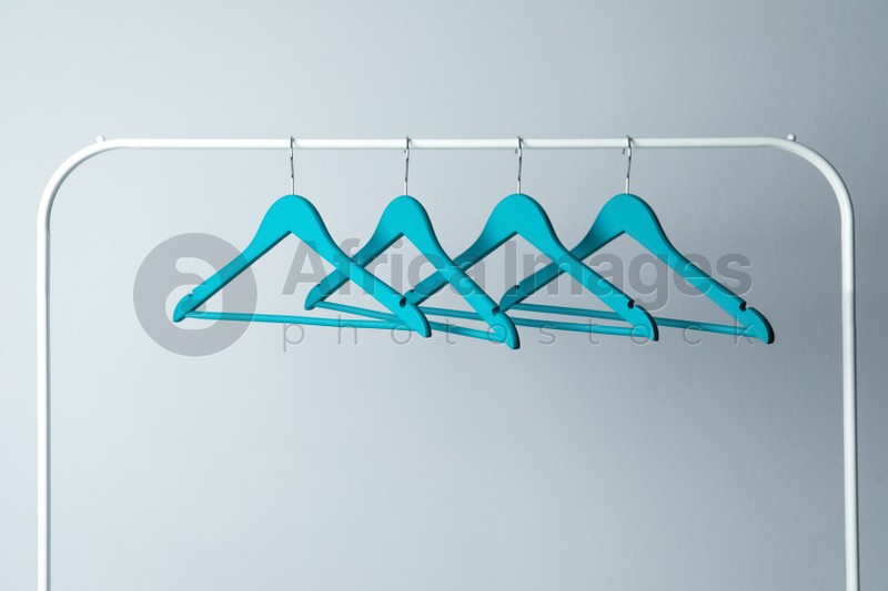 Photo of Empty turquoise clothes hangers on metal rack against light grey background