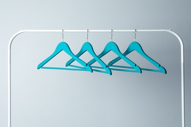 Empty turquoise clothes hangers on metal rack against light grey background