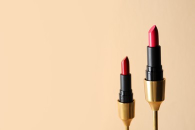 Photo of Beautiful glossy lipsticks on beige background, space for text