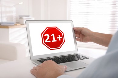 Man using laptop with age limit sign 21+ years indoors, closeup