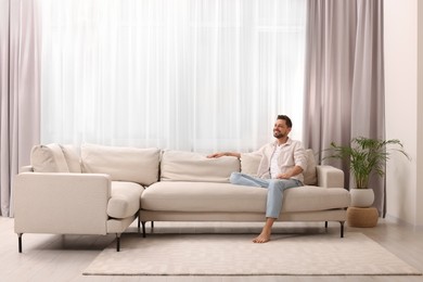 Happy man resting on sofa near window with beautiful curtains in living room