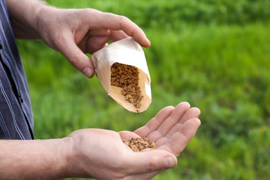Man pouring beet seeds from paper bag into hand outdoors, closeup