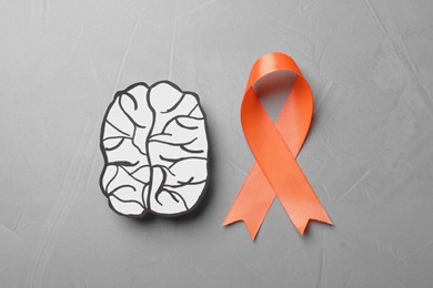 Orange ribbon and paper brain cutout on light grey table, flat lay. Multiple sclerosis awareness