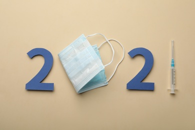 Paper numbers, medical mask and syringe forming 2021 on beige background, flat lay. Coronavirus vaccination