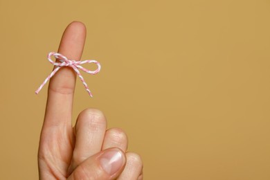 Woman showing index finger with tied bow as reminder on light brown background, closeup. Space for text