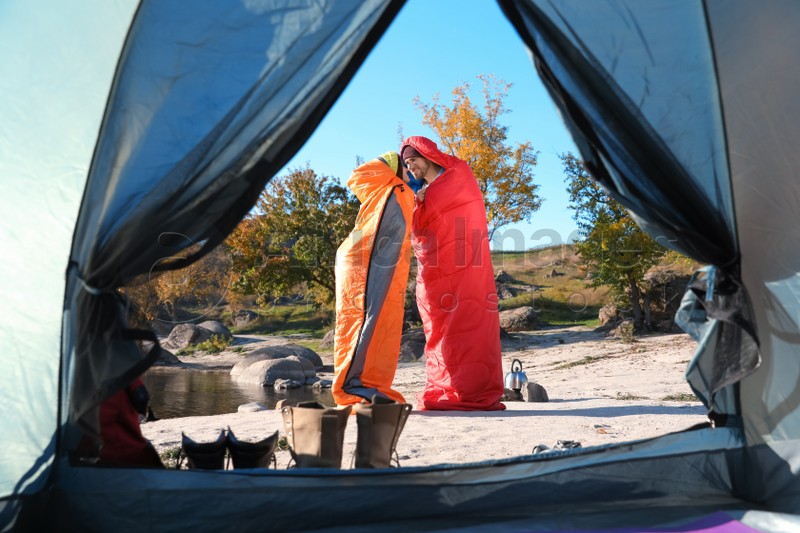 Cute couple in sleeping bags outdoors, view from camping tent
