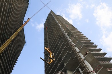 Tower crane near unfinished buildings against cloudy sky on construction site, low angle view
