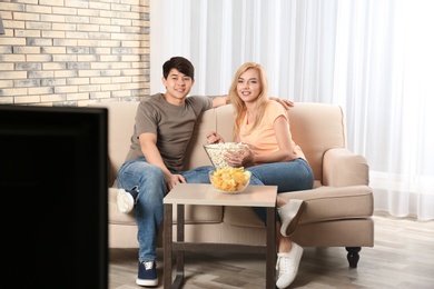 Young couple with snacks watching TV on sofa at home