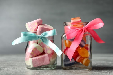 Tasty sweets in glass jars on light grey table, closeup
