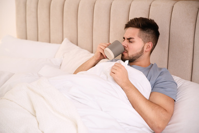 Sick young man with cup of hot drink in bed at home. Influenza virus