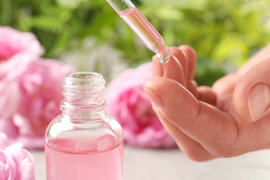 Woman dripping rose essential oil on finger near bottle, closeup