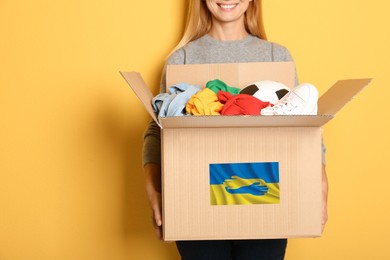 Humanitarian aid for Ukrainian refugees. Woman holding box with donations on color background. Space for text