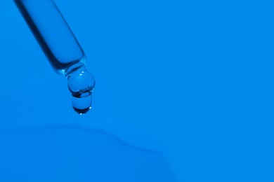 Dripping face serum from pipette on blue background, closeup. Space for text