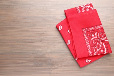 Folded red bandana with paisley pattern on wooden table, top view. Space for text