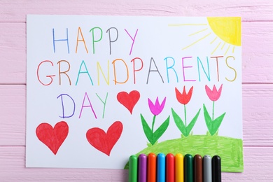 Beautiful drawing with phrase Happy Grandparents Day on pink wooden table, flat lay