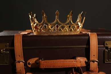 Beautiful golden crown on suitcase against black background. Fantasy item