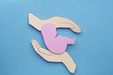 Photo of Hands with newborn paper figure on light blue background, flat lay. Woman`s health
