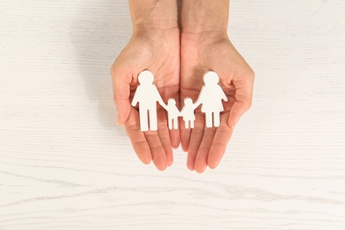 Woman holding figures of family in hands on white wooden background, top view