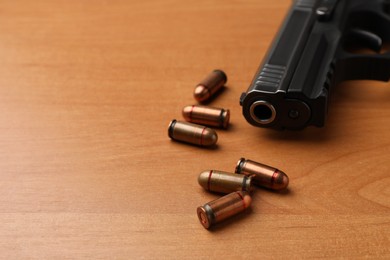 Semi-automatic pistol and bullets on wooden table, closeup. Space for text