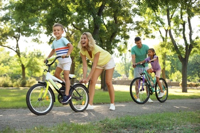 Happy parents teaching their children to ride bicycle in park