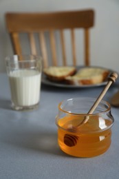 Photo of Jar with honey, milk and bread served for breakfast on grey table