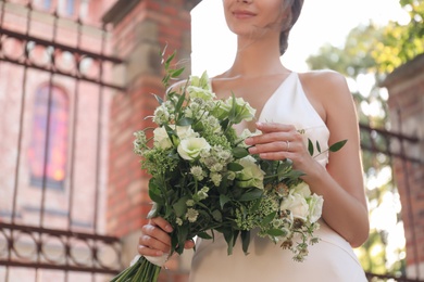 Gorgeous bride in beautiful wedding dress with bouquet near church, closeup