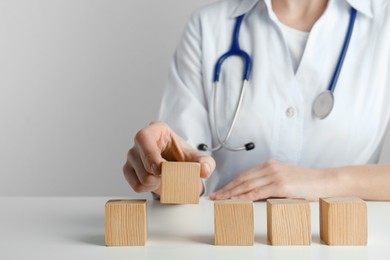 Photo of Doctor arranging blank wooden cubes on white table against light background, closeup. Space for text