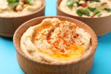 Bowl of tasty hummus with paprika on blue background, closeup