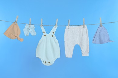Different baby clothes drying on laundry line against light blue background