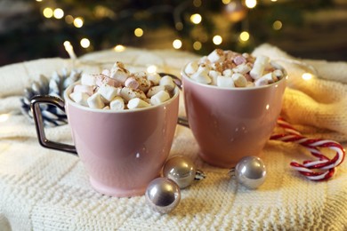 Photo of Cups of tasty cocoa with marshmallows, candy canes and Christmas decor on knitted plaid indoors