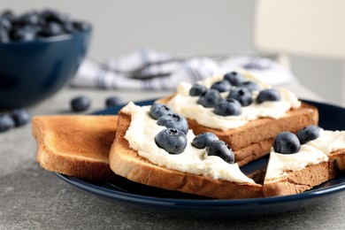 Tasty sandwiches with cream cheese and blueberries on grey table, closeup
